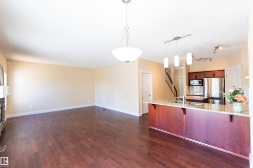 Open concept living space featuring wood-finish flooring, a stone fireplace, and a kitchen island with pendant lighting - 1419 Chahley Place Nw, Edmonton, AB 