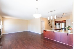 Open concept living space featuring wood-finish flooring, a stone fireplace, and a kitchen island with pendant lighting - 