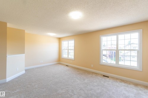 Spacious room with plush carpeting, two large windows, white trim, and neutral-toned walls - 1419 Chahley Place Nw, Edmonton, AB 