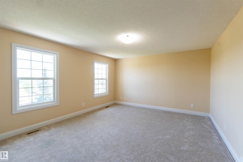 Spacious room featuring neutral carpeting, light-toned walls, two large windows, and a flush-mount ceiling light - 1419 Chahley Place Nw, Edmonton, AB 