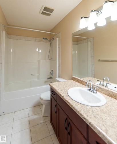 Tiled flooring complements a white bathtub and shower surround with a tiled accent border - 1419 Chahley Place Nw, Edmonton, AB 