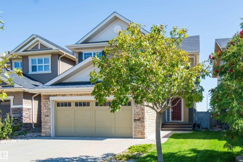Two-story residence featuring a two-car garage, stone and siding exterior, red entry door, and a manicured front lawn - 1419 Chahley Place Nw, Edmonton, AB 