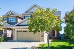 Two-story residence featuring a two-car garage, stone and siding exterior, red entry door, and a manicured front lawn - 