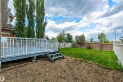 Expansive backyard featuring a manicured lawn, a raised wood deck with white railings, and a partial brick privacy fence - 