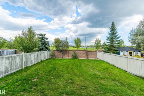 Expansive backyard featuring a green lawn, wood fencing, a brick retaining wall, and mature landscaping - 1419 Chahley Place Nw, Edmonton, AB 