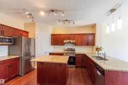 Kitchen featuring wood-finish flooring, wood cabinetry, stainless steel appliances, granite countertops, and an island - 