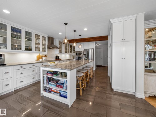 Gourmet kitchen featuring white cabinetry, glass-front upper cabinets, a large island with built-in shelving, stainless steel appliances, and wood-look flooring - 1223 Appleton Close, Sherwood Park, AB 