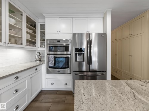 White shaker cabinetry, stainless steel appliances, built-in double ovens, light-toned stone countertops, and wood-finish flooring - 1223 Appleton Close, Sherwood Park, AB 