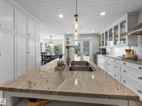 Kitchen island with integrated double basin stainless steel sink, light-toned countertop, white shaker cabinetry, and glass pendant lighting - 1223 Appleton Close, Sherwood Park, AB 