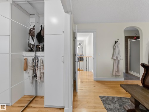 White built-in wardrobe with mirrored sliding doors, wood-finish flooring, and an arched doorway leading to a shower enclosure - 1223 Appleton Close, Sherwood Park, AB 
