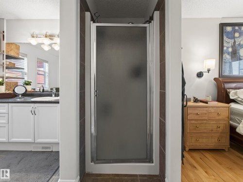 Frosted glass shower enclosure, white vanity with integrated sink, dark countertop, light wood-finish flooring, and a wall-mounted sconce - 1223 Appleton Close, Sherwood Park, AB 