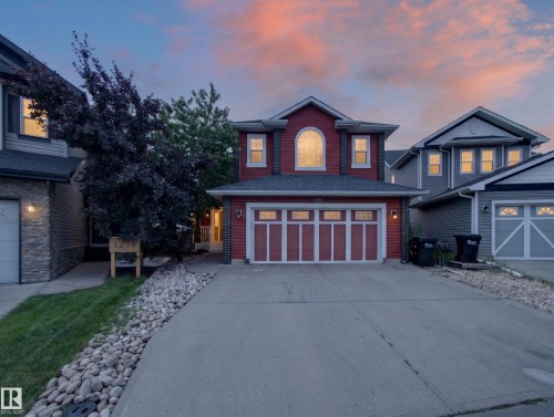 Red siding exterior with white trim, arched window detail, attached garage with panel doors, concrete driveway, and rock landscaping - 1223 Appleton Close, Sherwood Park, AB 