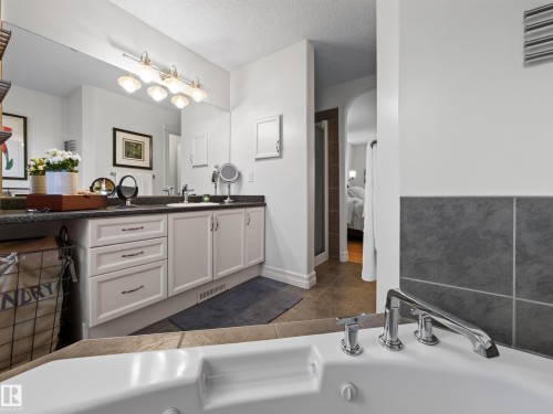 Built-in jetted tub with chrome fixtures, dual vanity with shaker-style cabinetry, dark countertop, and large wall-mounted mirror with overhead lighting - 1223 Appleton Close, Sherwood Park, AB 
