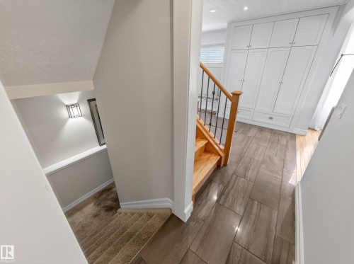 Staircase with wood treads and wrought iron balusters, tile flooring, built-in white cabinetry, and a wall-mounted sconce - 1223 Appleton Close, Sherwood Park, AB 