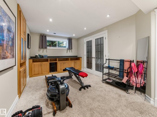 Recessed lighting, light-colored carpeting, built-in wooden cabinetry with glass-front storage, and double French doors with frosted glass panels - 1223 Appleton Close, Sherwood Park, AB 