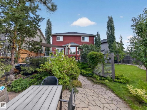 Expansive backyard featuring a stone-paved pathway, mature landscaping, and a red-sided structure with multiple windows - 1223 Appleton Close, Sherwood Park, AB 