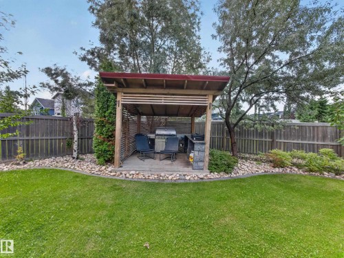 Landscaped backyard featuring a wooden pergola with a red roof, a manicured lawn, and a stone-edged garden bed - 1223 Appleton Close, Sherwood Park, AB 