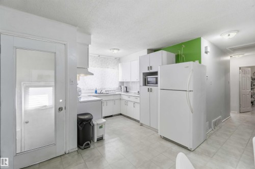 Kitchen featuring white cabinetry, white appliances, a tile floor, and a corner sink - 13408 67 Street Nw, Edmonton, AB 