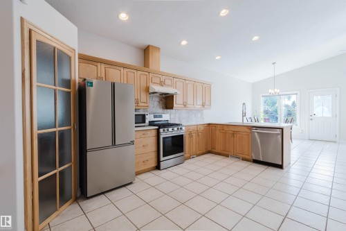 Kitchen featuring light wood cabinetry, stainless steel appliances, and white tile flooring - 8517 156 Avenue Nw, Edmonton, AB 