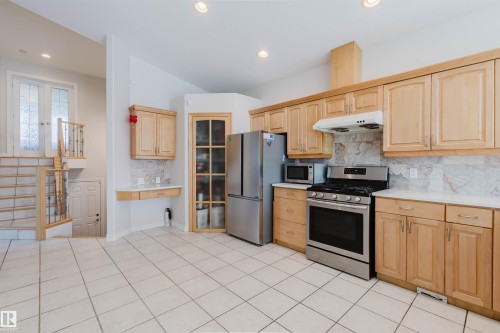 Kitchen featuring stainless steel appliances, light wood-finish cabinetry, tile flooring, white countertops, and a full tile backsplash - 8517 156 Avenue Nw, Edmonton, AB 