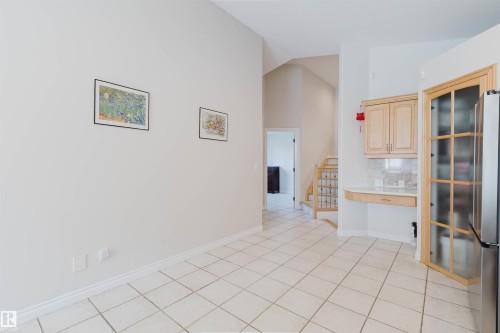 Vaulted ceilings, light-toned tile flooring, built-in cabinetry with glass-front display, staircase with wood newel posts, and a built-in desk area - 8517 156 Avenue Nw, Edmonton, AB 