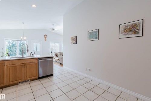 Kitchen area featuring wood cabinetry, stainless steel dishwasher, an undermount sink with a gooseneck faucet, and light-toned tile flooring - 8517 156 Avenue Nw, Edmonton, AB 