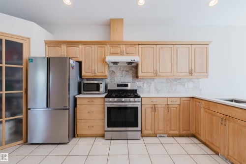 Kitchen featuring light wood cabinetry, stone countertops, stainless steel appliances, and a tiled floor - 8517 156 Avenue Nw, Edmonton, AB 