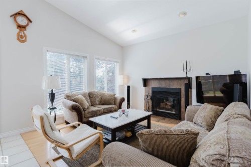 Vaulted ceiling, recessed lighting, wood-finish flooring, large windows, and a built-in fireplace with a stone surround - 8517 156 Avenue Nw, Edmonton, AB 