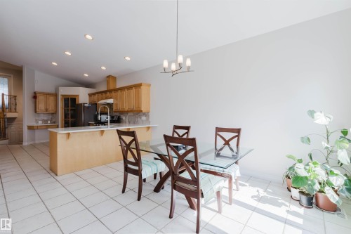 Kitchen featuring a built-in kitchen island with a white countertop and natural wood cabinetry, a stainless steel refrigerator, and a stainless steel sink with a high-arch faucet - 8517 156 Avenue Nw, Edmonton, AB 