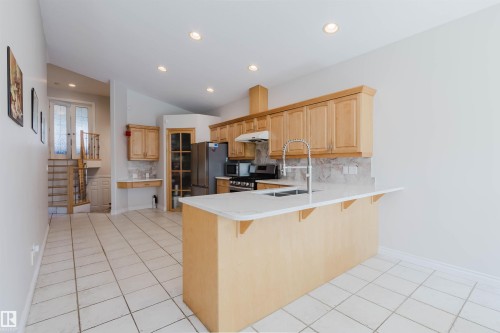 Kitchen featuring light wood cabinetry, white stone countertops, stainless steel appliances, and a tiled backsplash - 8517 156 Avenue Nw, Edmonton, AB 