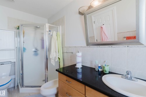 Glass-enclosed shower, light wood-finish vanity with dark countertop, integrated sink, and wall-mounted mirror - 8517 156 Avenue Nw, Edmonton, AB 