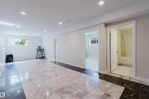 Recessed lighting illuminates the expansive room featuring large-format tile flooring with a contrasting border, and multiple windows - 8517 156 Avenue Nw, Edmonton, AB 