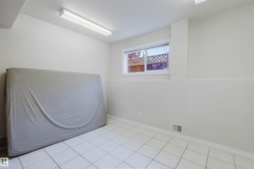 White tile flooring, white painted walls, white trim, fluorescent lighting, and a window with a latticework fence visible - 8517 156 Avenue Nw, Edmonton, AB 