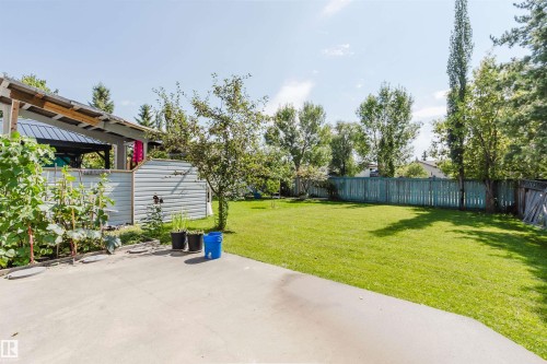 Expansive concrete patio with a covered pergola, adjacent garden bed, large grassy area, and a wood privacy fence - 8517 156 Avenue Nw, Edmonton, AB 