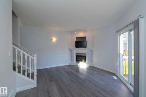 Wood-finish flooring, corner fireplace with white mantel, white staircase with balusters, wall-mounted sconce, and sliding glass door - #37 3811 85 St Nw, Edmonton, AB 