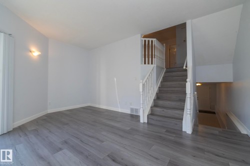Wood-finish flooring, white walls, white trim, white staircase with balusters, and a wall-mounted light fixture - #37 3811 85 St Nw, Edmonton, AB 