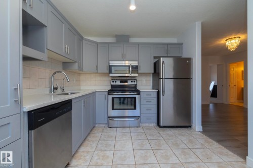 Kitchen featuring gray cabinetry, stainless steel appliances, light-toned countertop, square tile backsplash, and ceramic tile flooring - #37 3811 85 St Nw, Edmonton, AB 
