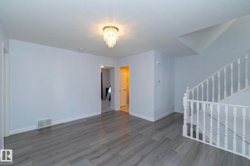 Wood-finish flooring, white painted walls, white trim, and an overhead chandelier with decorative accents - #37 3811 85 St Nw, Edmonton, AB 
