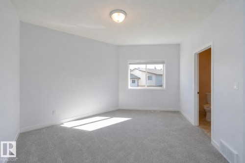Neutral wall color, light-toned carpeting, ceiling-mounted light fixture, window with exterior views, and an interior door - #37 3811 85 St Nw, Edmonton, AB 
