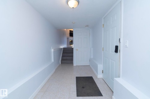 Foyer featuring light-toned tile flooring, white paneled doors, and a staircase with a half-wall railing - #37 3811 85 St Nw, Edmonton, AB 