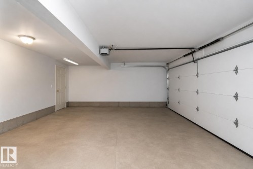 Spacious garage with light-colored concrete flooring, white paneled garage door, and a single entry door - #37 3811 85 St Nw, Edmonton, AB 