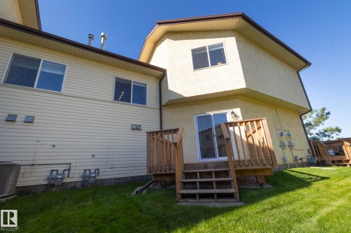 Rear exterior with a wooden deck, sliding glass door, and a grass lawn - #37 3811 85 St Nw, Edmonton, AB 