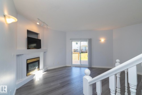 Built-in fireplace with a decorative mantel, wood-finish flooring, sliding glass patio door, and white painted balusters - #37 3811 85 St Nw, Edmonton, AB 