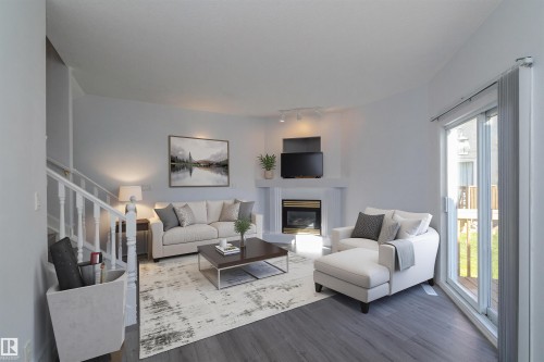 White fireplace with a dark insert, track lighting, light gray walls, wood-finish flooring, and white stair railing - #37 3811 85 St Nw, Edmonton, AB 