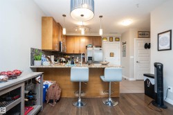 Open-concept kitchen featuring wood-finish flooring, light wood cabinetry, stainless steel appliances, and a tiled backsplash - 