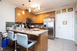 Kitchen featuring wood cabinetry, stainless steel appliances, a mosaic tile backsplash, and a granite-finish countertop with an integrated breakfast bar - 