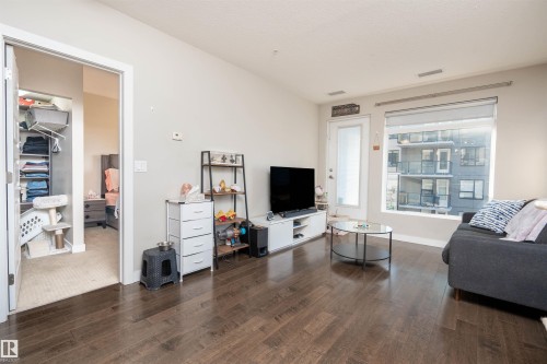 Spacious living area featuring wood-finish flooring, light-colored walls, and a large window - #610 5151 Windermere Bv Sw, Edmonton, AB - Indoor Photo Showing Living Room