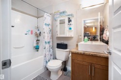 Bathroom featuring a white bathtub with shower, a vanity with a surface-mounted sink, a vanity mirror, wood-finish cabinetry, and a toilet - 