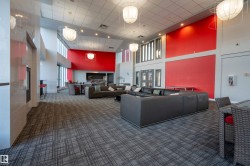 Spacious common area featuring high ceilings, contemporary pendant lighting, patterned carpeting, a full-height red accent wall, and extensive natural light from large windows - 
