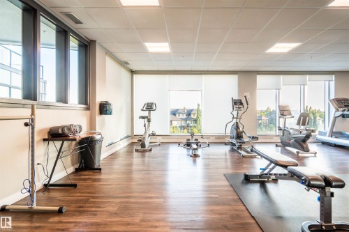 Dedicated fitness room featuring wood-finish flooring and multiple exercise machines - #610 5151 Windermere Bv Sw, Edmonton, AB - Indoor Photo Showing Gym Room